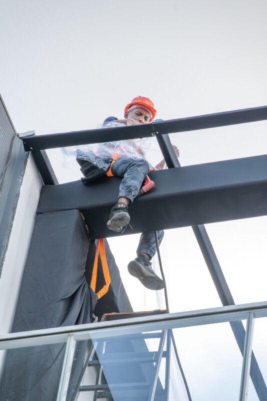 Profissional com cinto de segurança e capacete em trabalho em altura sobre estrutura metálica