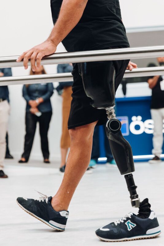 Usuário caminhando com prótese de perna entre barras paralelas