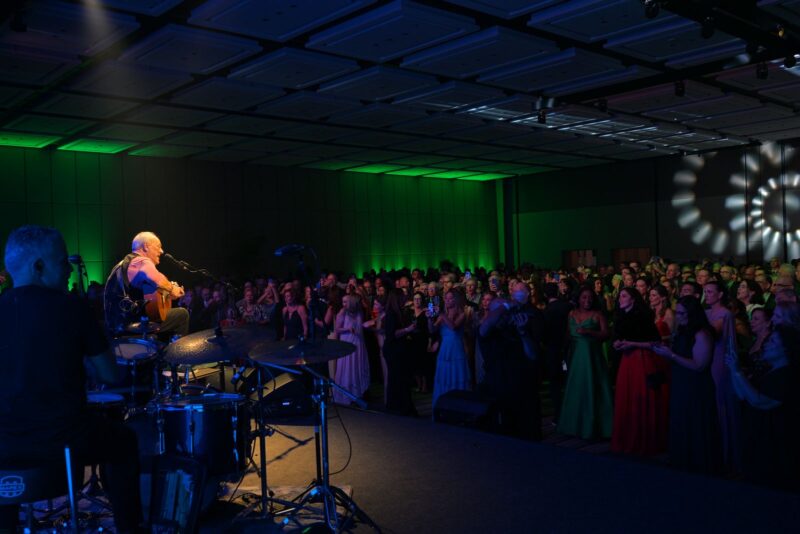 Cantor Toquinho se apresentando no palco para a plateia na Festa do Centenário da SMCC, no Royal Palm Hall