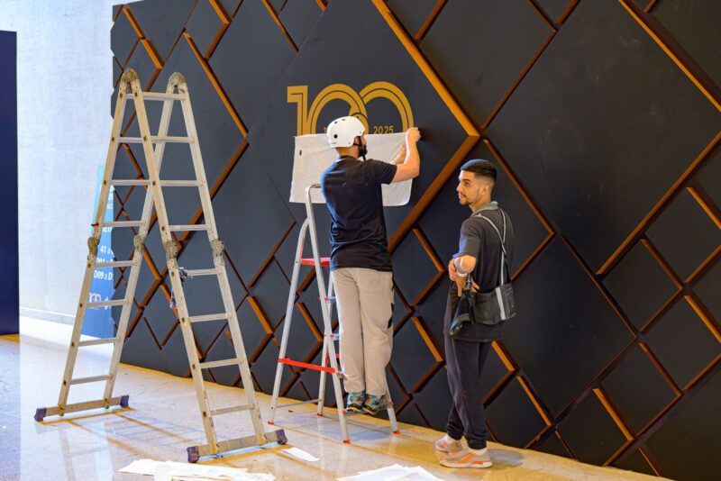 Profissionais da BlueTie montando o painel do centenário no cenário da Festa do Centenário da SMCC