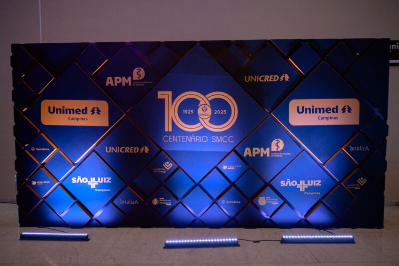 Painel de patrocinadores iluminado em azul com o logo do centenário na Festa do Centenário da SMCC